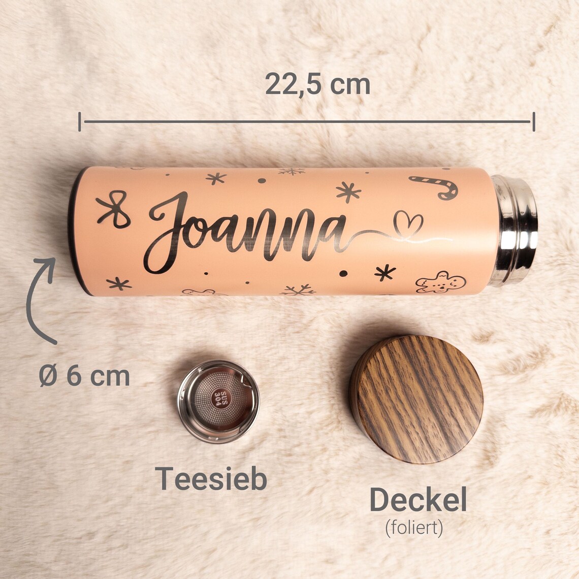 Pfirsichfarbene personalisierte Thermosflasche „Joanna“ aus Edelstahl, liegend auf weißem Fell, mit eingezeichneten Maßen 22,5 cm Länge und 6 cm Durchmesser; darunter separat abgebildet ein herausnehmbares Teesieb aus Edelstahl und ein Holzoptik-Deckel mit Beschriftungen „Teesieb“ und „Deckel (foliert)“.