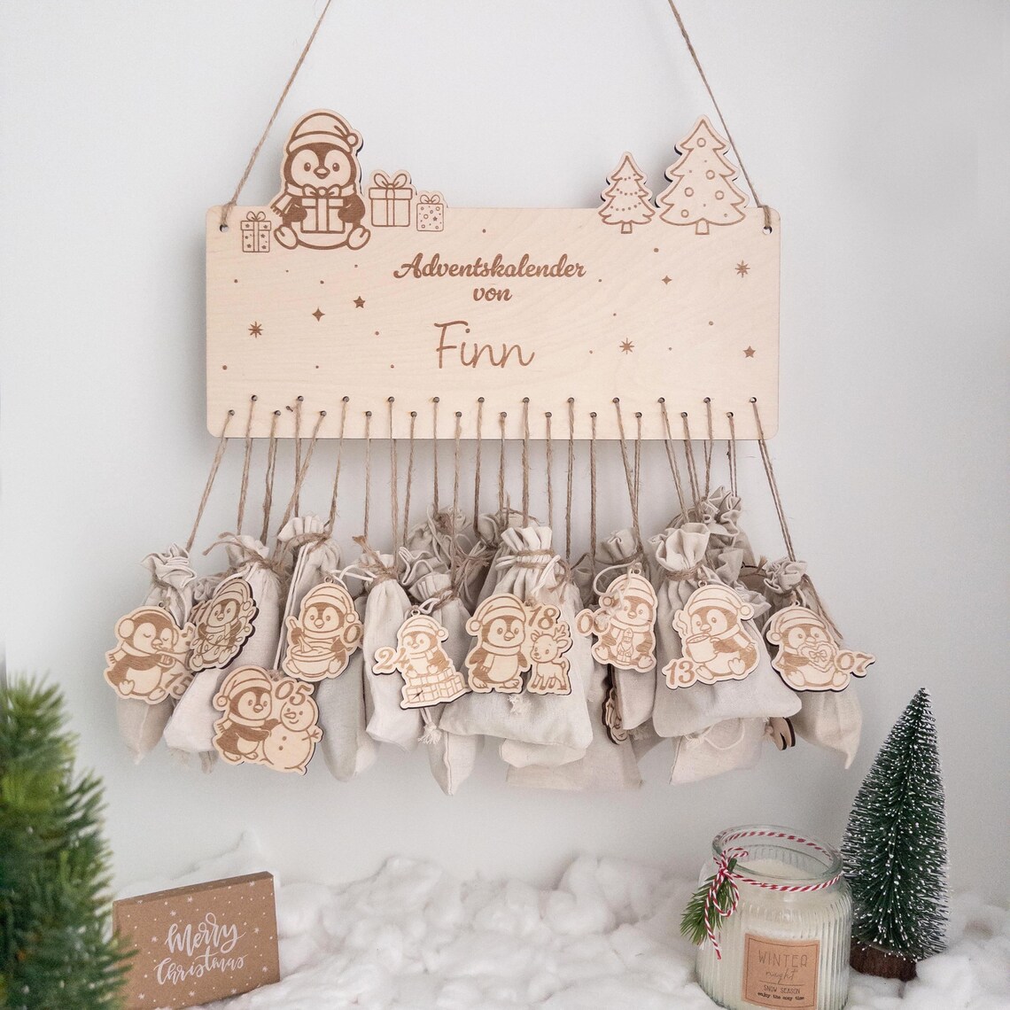 Personalisierter Adventskalender aus Holz mit Name ‚Finn‘, niedlichen Pinguin- und Tannen-Motiven, 24 Jutebeuteln und nummerierten Holzanhängern – skandinavische Weihnachtsdeko zum Aufhängen.