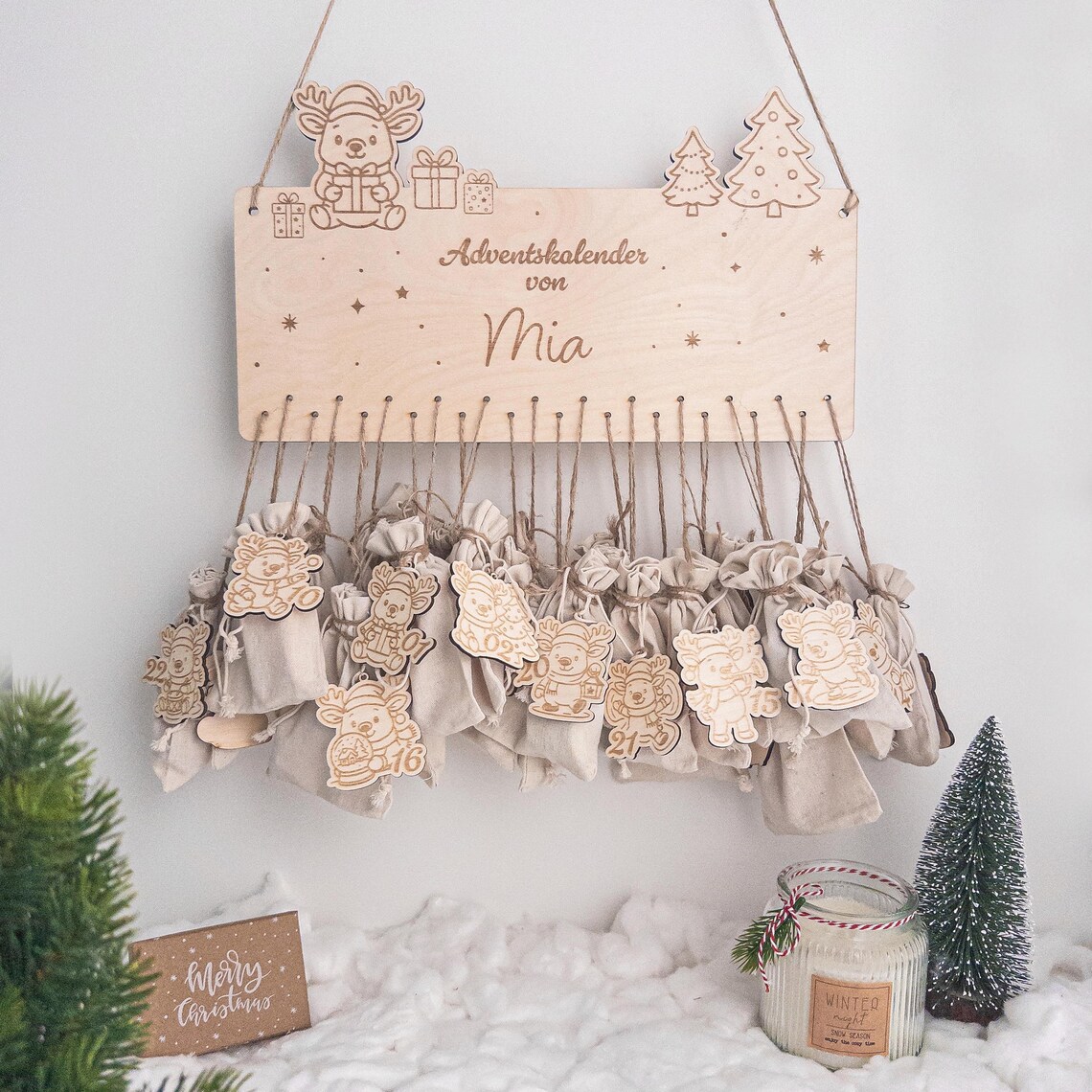 Personalisierter Adventskalender aus Holz mit Name ‚Mia‘, süßem Rentier und Tannen, 24 Jutebeuteln und nummerierten Holzanhängern – skandinavische Weihnachtsdeko zum Aufhängen.