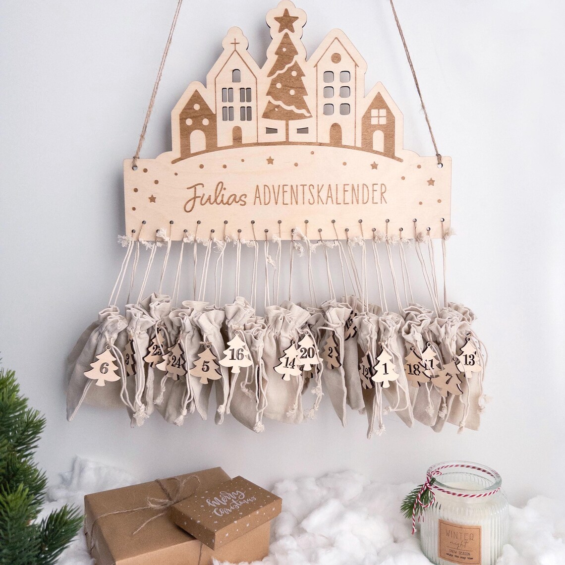 Personalisierter Adventskalender aus Birkenholz mit Häuser- und Baumdesign, Namensgravur, 24 Stoffbeutel mit nummerierten Anhängern 1–24, skandinavische Weihnachtsdeko.