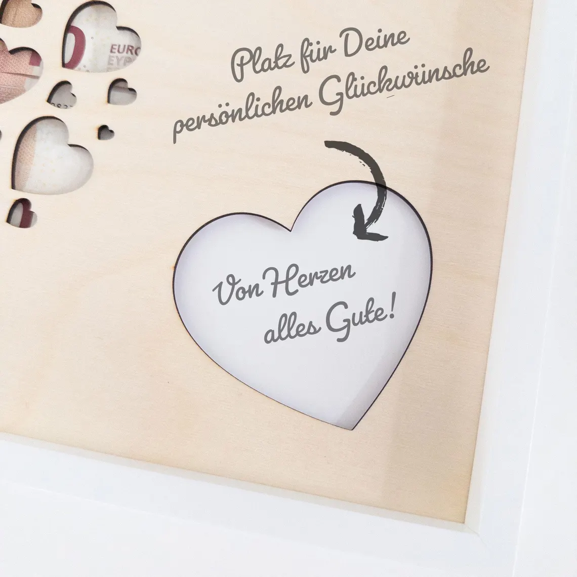 Eine Bilderrahmen mit herzförmigen Ausschnitten und dem Text "Platz für Deine persönlichen Glückwünsche" und "Von Herzen alles Gute!" in einem weißen Rahmen. Das Holz ist hellbraun.